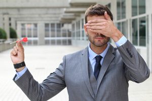 Man covering his eyes throwing a dart