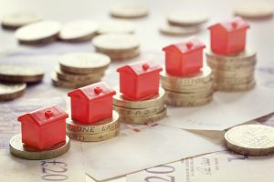 Image of miniature houses stacked on money, representing profits from lending to mortgage holders