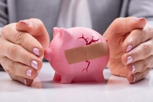 Image of a businesswoman protecting a wounded and bandaged piggy bank