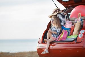 Image of a little girl sitting in the trunk of a car during a summer road trip