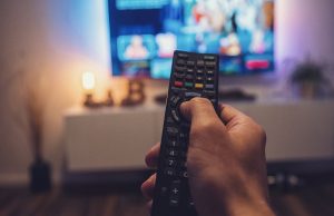 Image of a man holding a T.V. remote while watching news of a coming recession