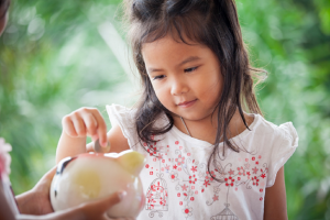 Image of a young girl learning savings habits by using a piggy bank