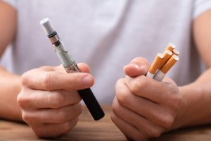 Image of a man holding a vape pen and cigarettes