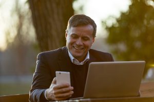 Image of a senior man using his laptop and smartphone for short-term trading