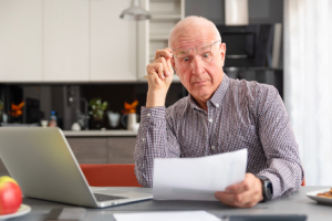 Image of an amazed senior man reading a sheet of paper in his kitchen