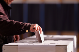 Image of a middle-aged voter submitting their ballot into a white box