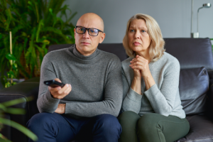 Image of a concerned middle-aged couple watching the news in their living room