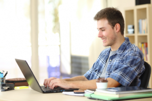 Image of a teen boy at a desk writing an email on his laptop