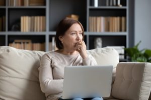 Image of a pensive senior woman thinking while holding her laptop