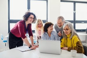 Image of several happy seniors crowding around a laptop centered between them on a desk in an office