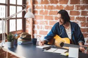 Image of a young man writing a song with his guitar