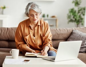 Image of a senior woman with a laptop and notebook