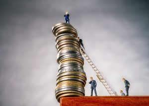 Image of miniature bankers teetering on a dangerously high stack of coins