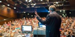 Image from behind of a male speaker presenting at a conference