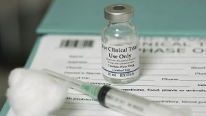 Image of a vial of clinical trial medicine and a syringe over trial forms