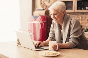 Image of a happy senior woman reading on her laptop while holding a cup of tea