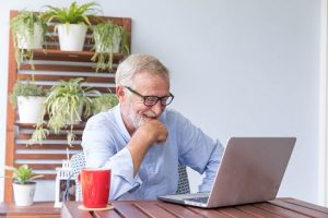 Image of a happy senior man looking at his laptop with plants in the background