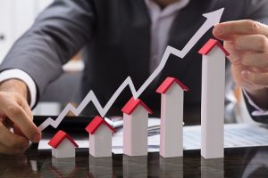 Image of a businessman holding a paper graph over model houses, representing profits from real estate