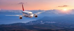 Image of an airplane flying over mountains at sunset