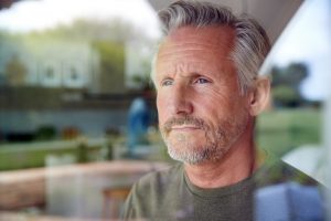 Image of an unsure senior man looking out his kitchen door