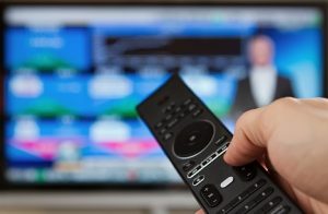 Image of a remote in front of a television screen showing stock market news