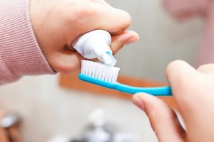 Image of a pair of hands applying toothpaste to a toothbrush in a bathroom