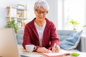 Image of a happy senior woman taking notes from her computer