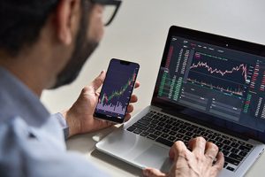 Man using phone and laptop to track stocks