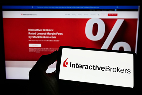 Image of a person holding phone with Interactive Brokers logo in front of company website
