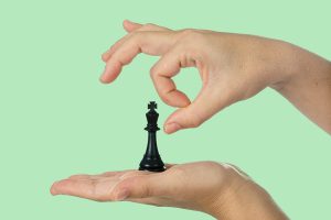 A hand about to topple a “king” chess piece