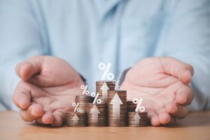 Two hands holding several piles of coins with arrows and percent signs on them