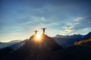 Two people’s silhouettes standing at the peak of a mountain