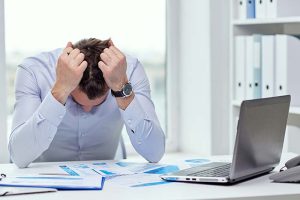 A stressed businessman sitting at his desk with his hands on his head