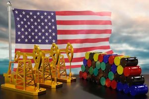 A line of oil pumps and a pile of oil barrels in front of an American flag