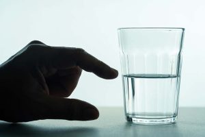 A hand next to a half-full (or half-empty) glass of water