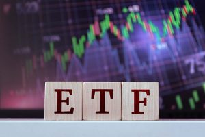 The letters “ETF” spelled out on blocks in front of a stock chart