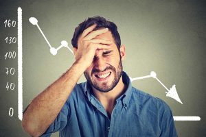 A frustrated man with his hand on his head, standing in front of a declining stock chart
