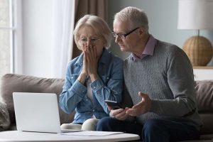 A distressed elderly couple sitting in front of their computer
