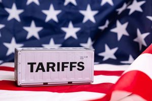 The word “tariffs” on a container in front of an American flag background