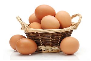 A basket containing about 10 brown eggs, with three more eggs lying on the ground next to it