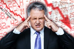 A frustrated male investor with his hands on his head and numerous red, downward-facing arrows in the background.
