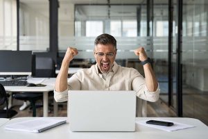 A middle-aged man sitting at his computer and shouting in excitement