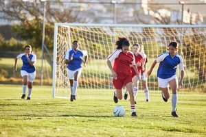 Six teenage girls in red and blue jerseys playing soccer