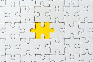 Several white puzzle pieces put together, with a yellow space in the middle where the last piece should be