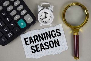 The words “earnings season” written on a slip of paper next to a calculator, a clock, and a magnifying glass