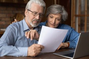 A retirement-age couple sitting at a desk and looking at a piece of paper