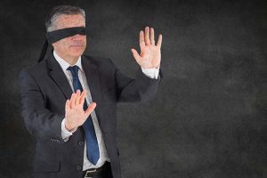 A middle-aged man blindfolded with his hands raised as if trying to feel his way around the room