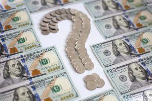 Coins arranged in the shape of a question mark, surrounded by dollar bills
