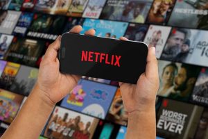 A smartphone with the Netflix logo in front of a grid of movie posters