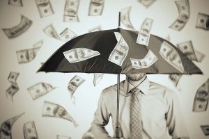 A businessman standing under an umbrella as dollar bills fall around him